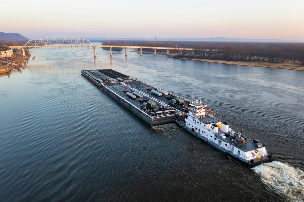 A large barge navigates the Mississippi River near a bridge in Wabasha, Minnesota.
